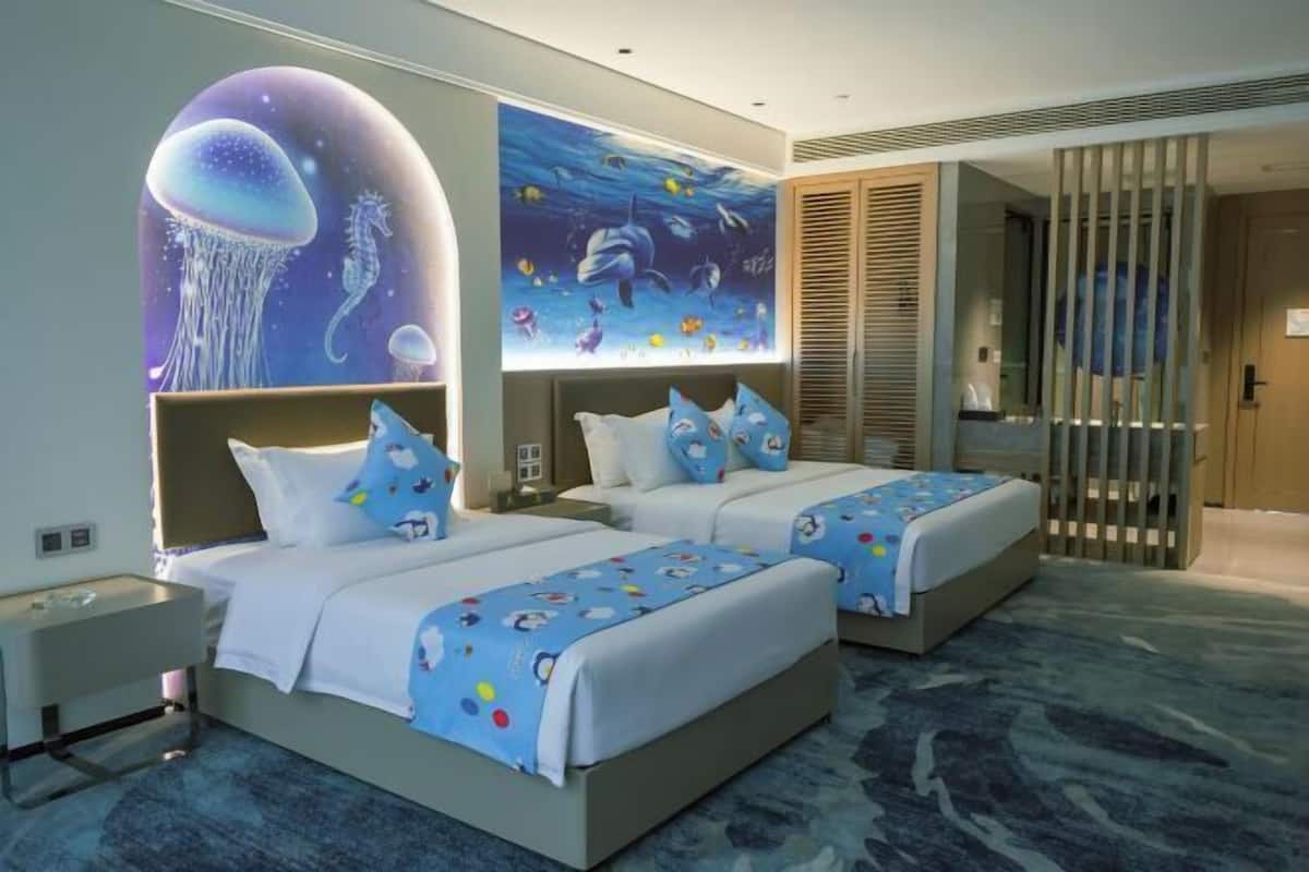 A hotel room with two beds, a large mural of ocean life, and a view of the sea through a sliding door.