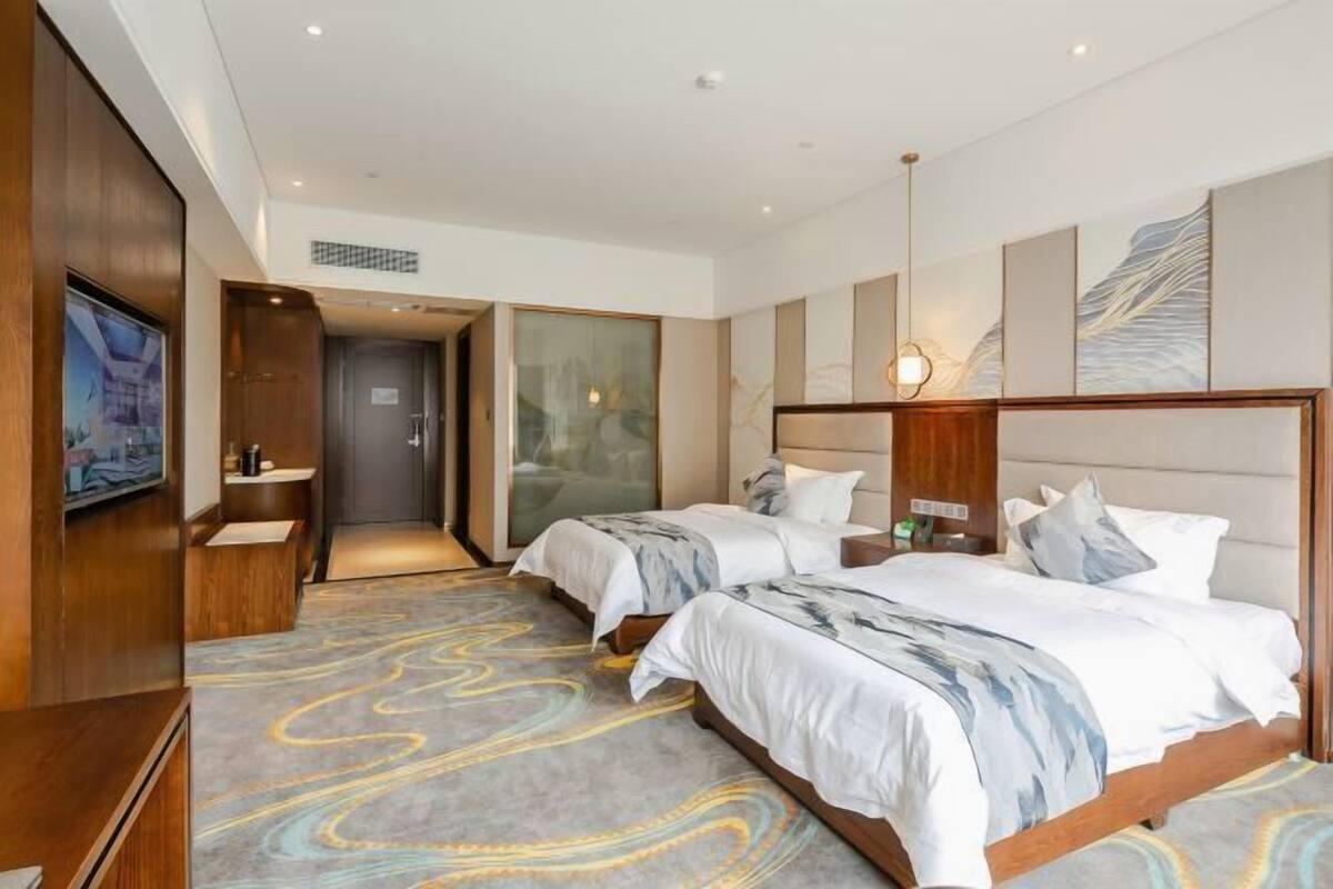 A hotel room with two beds, a TV, a bathroom, and a view of the city.