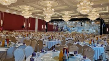 A banquet hall with round tables, chairs, and chandeliers.