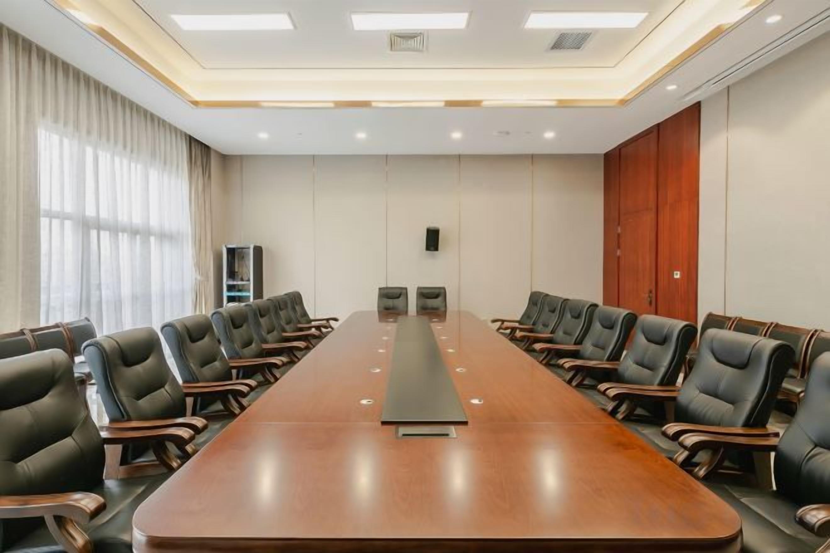 A conference room with a long table and chairs, a whiteboard, and a speaker on the wall.