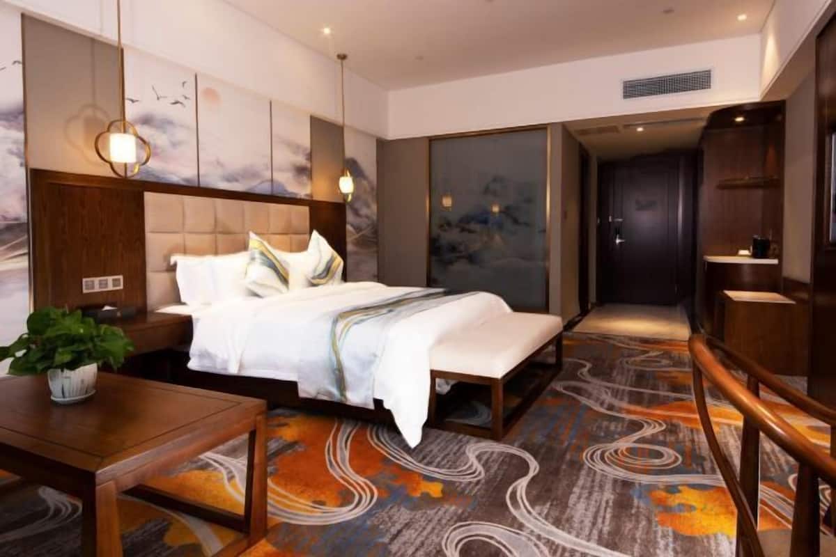 A hotel room with a bed, bedside table, and a potted plant.