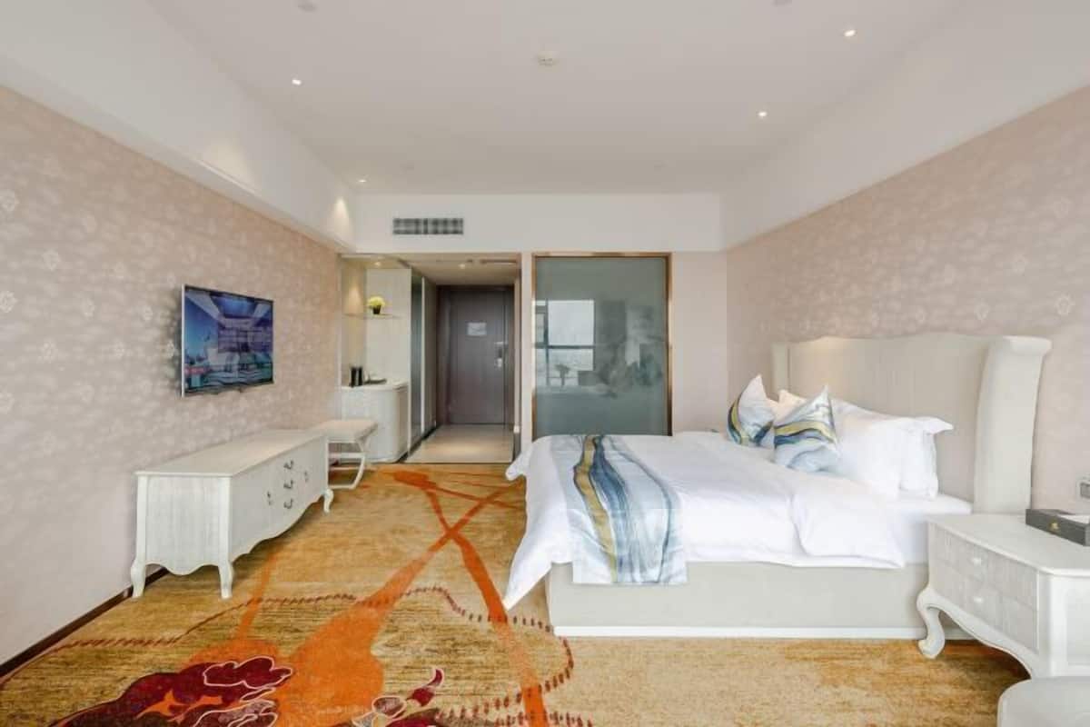 A hotel room with a bed, bedside tables, a desk, and a patterned carpet.