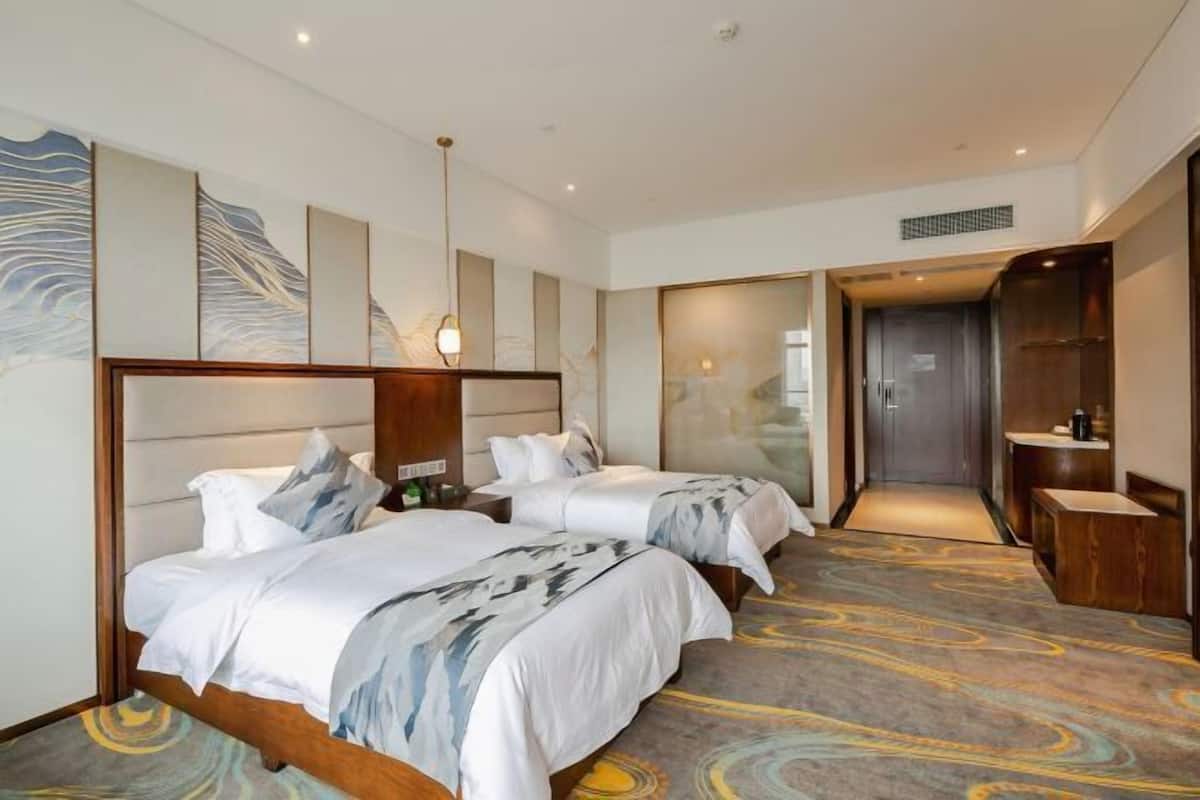 A hotel room with two beds, a large mirror, a bathroom with a sink, and a carpeted floor.