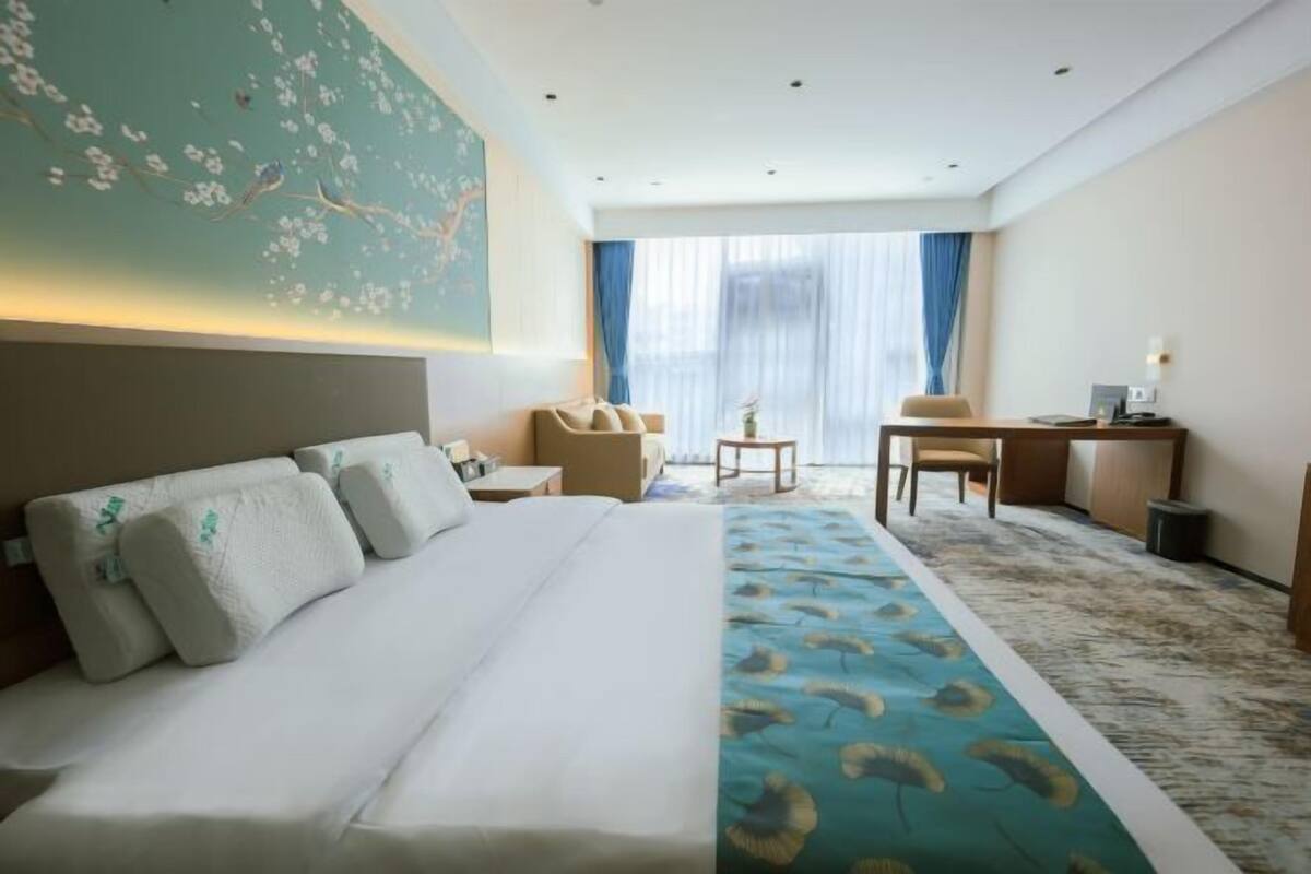 A hotel room with a large bed, a desk, a chair, and a small table.