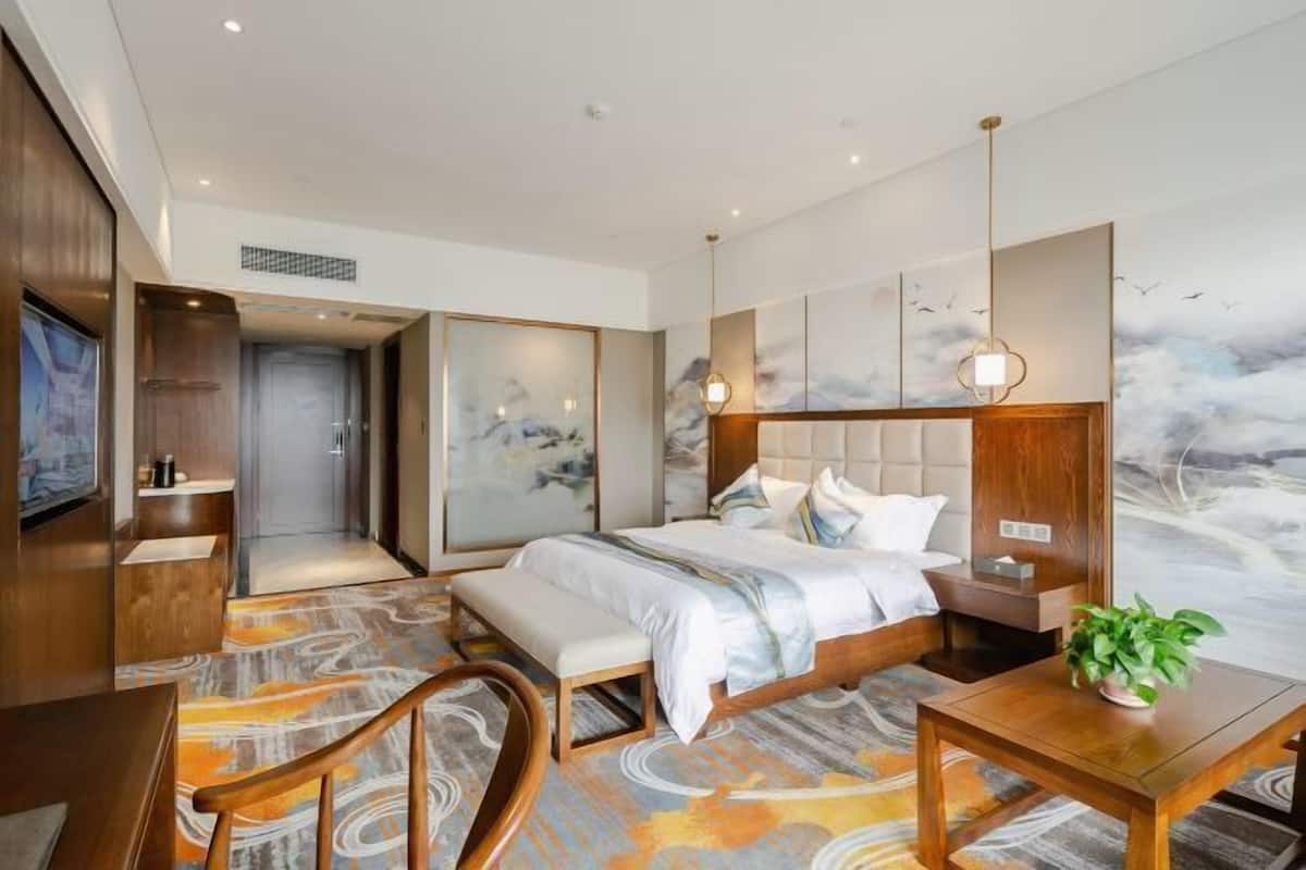 A modern hotel room with a bed, bedside table, chair, and a TV.