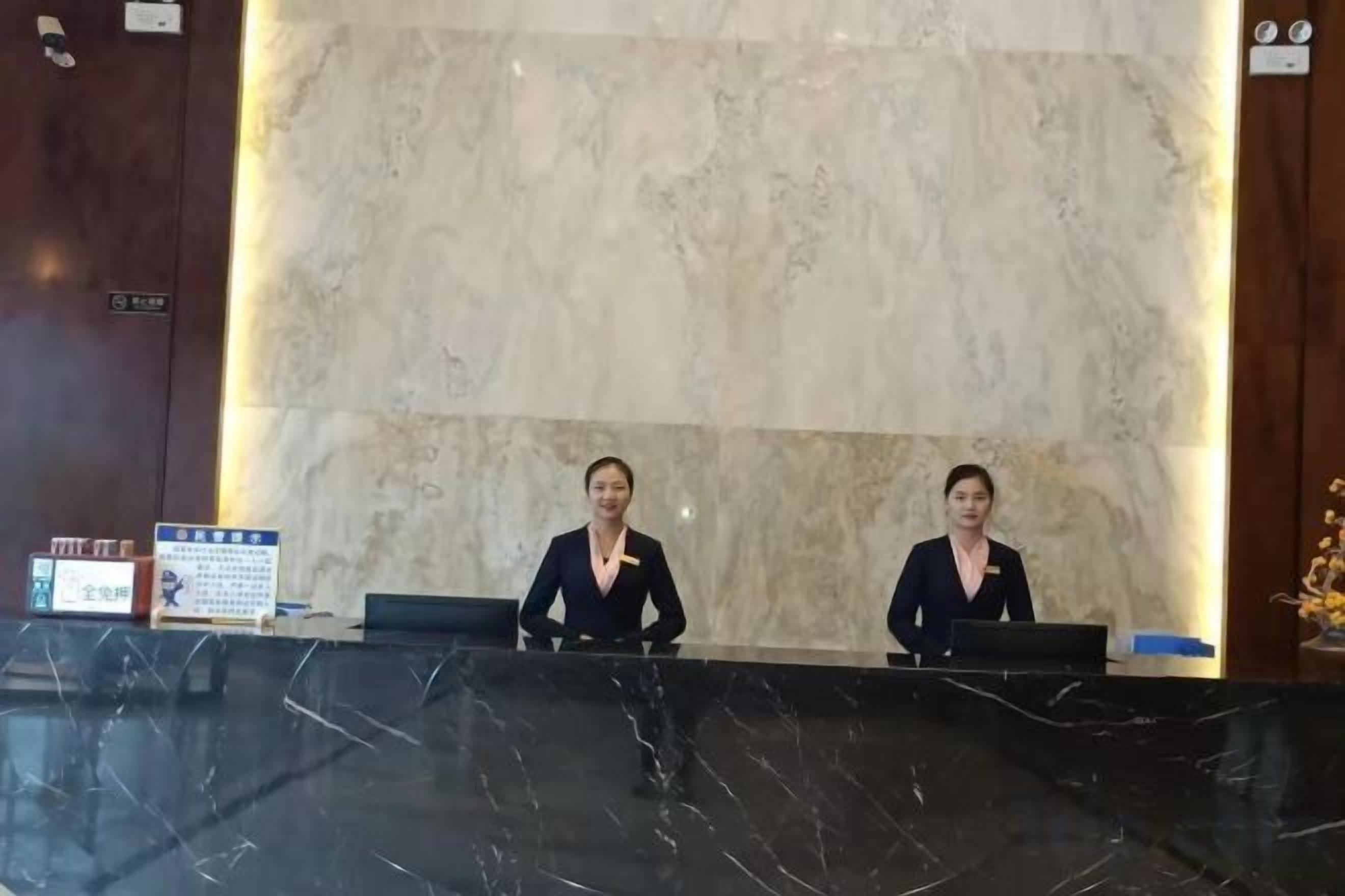 Una mesa de recepción con dos empleados, una pared de mármol y un cartel.