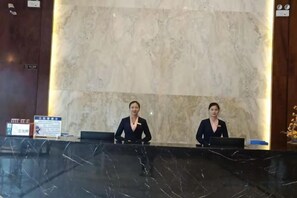 A reception desk with two staff members, a marble wall, and a signboard. - Yuhe Hotel (Jiajiang)