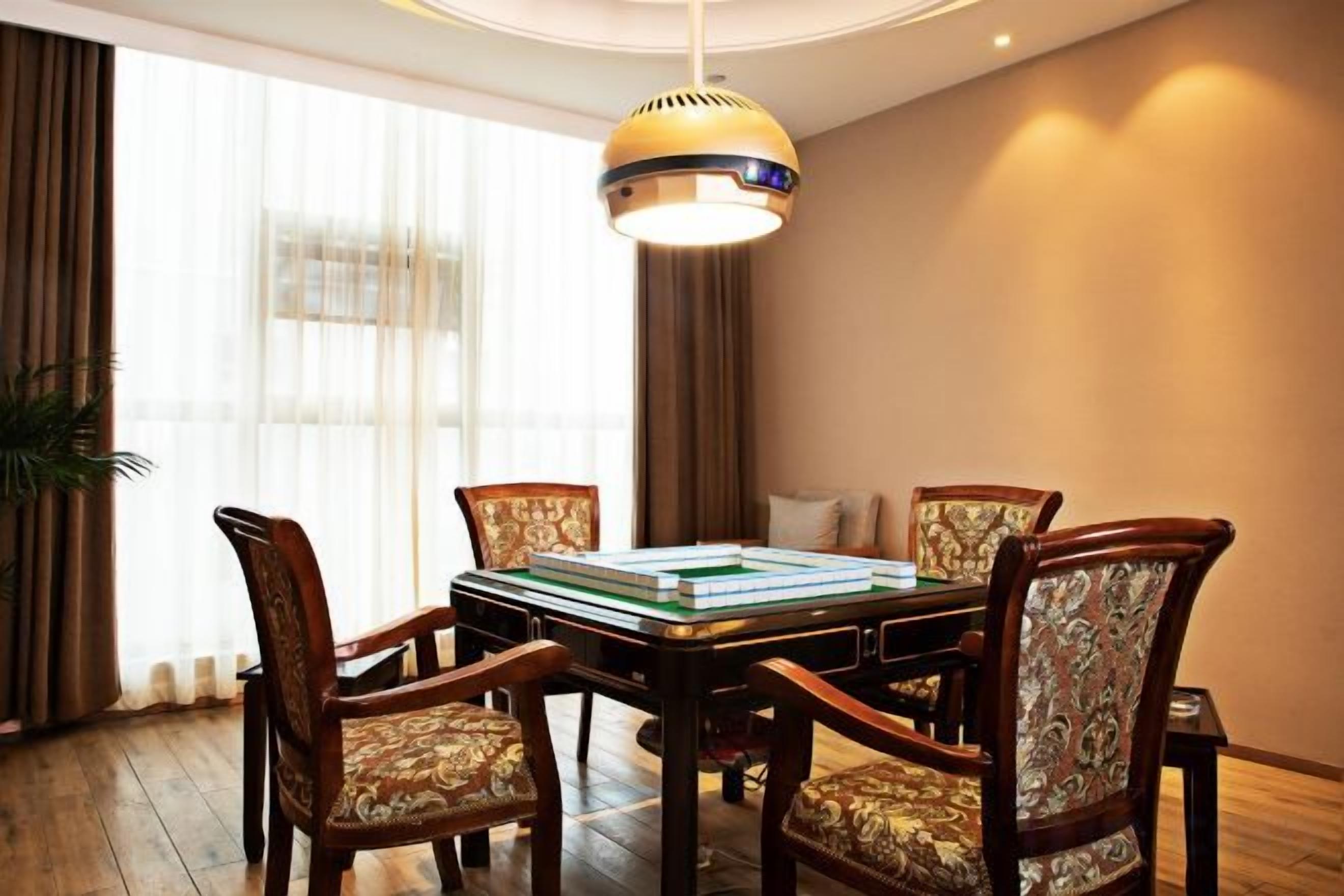 A dining area with a rectangular table surrounded by four upholstered chairs, a hanging light fixture above, and a large window with curtains.