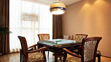 A dining area with a rectangular table surrounded by four upholstered chairs, a hanging light fixture above, and a large window with curtains.
