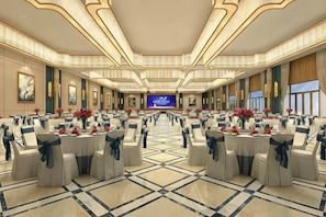 Une vaste salle de banquet avec des rangées de tables et de chaises, une scène à l’avant et un grand écran.