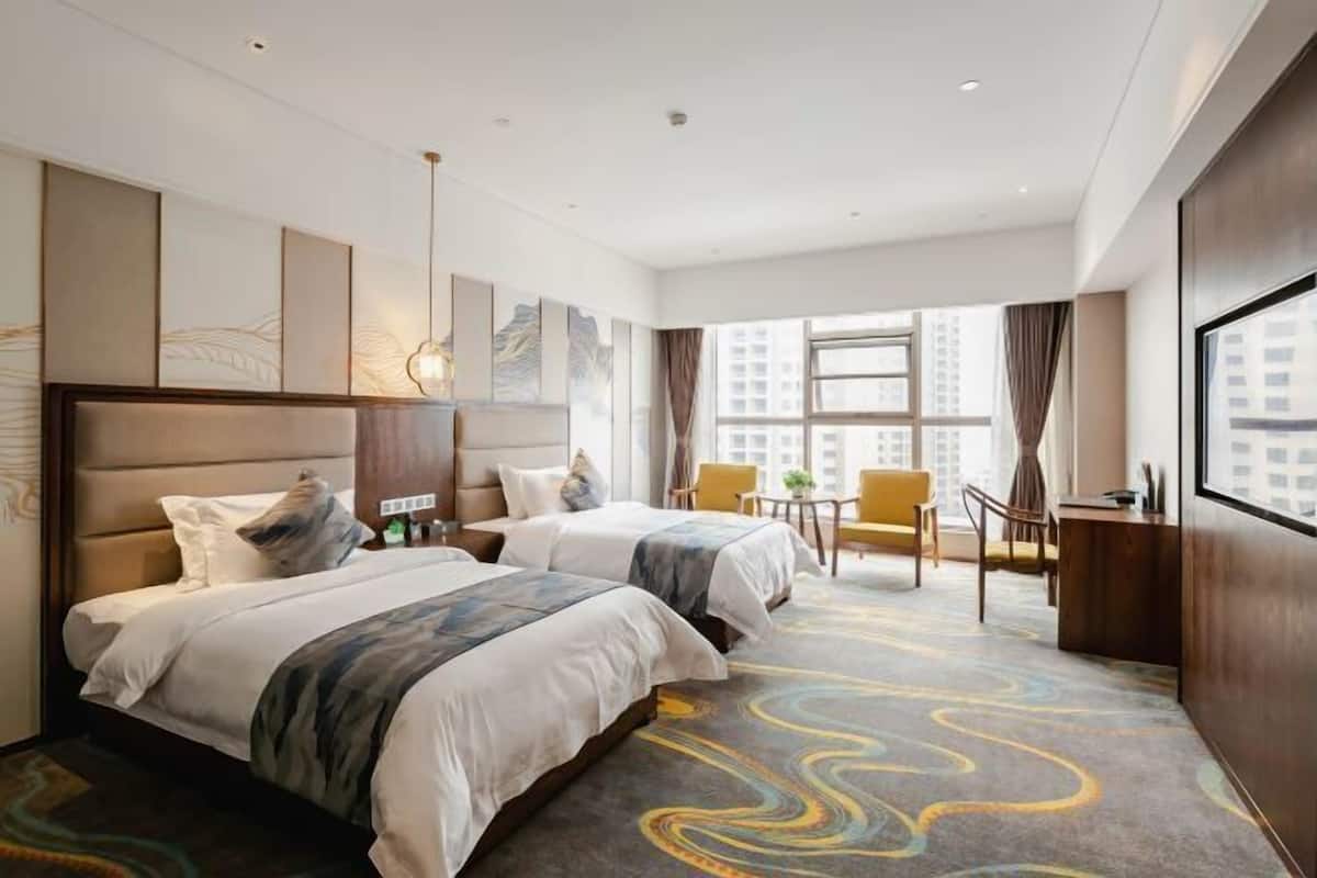 A hotel room with two beds, a desk, a chair, and a large window.