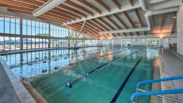 Una piscina interior con carriles delimitados, un alto techo de madera y ventanas amplias.