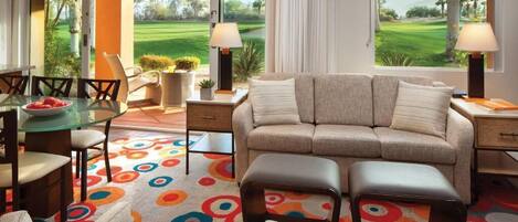 Una sala de estar moderna con un sofá, un reposapiés y sillones, una mesa de vidrio y una alfombra colorida.
