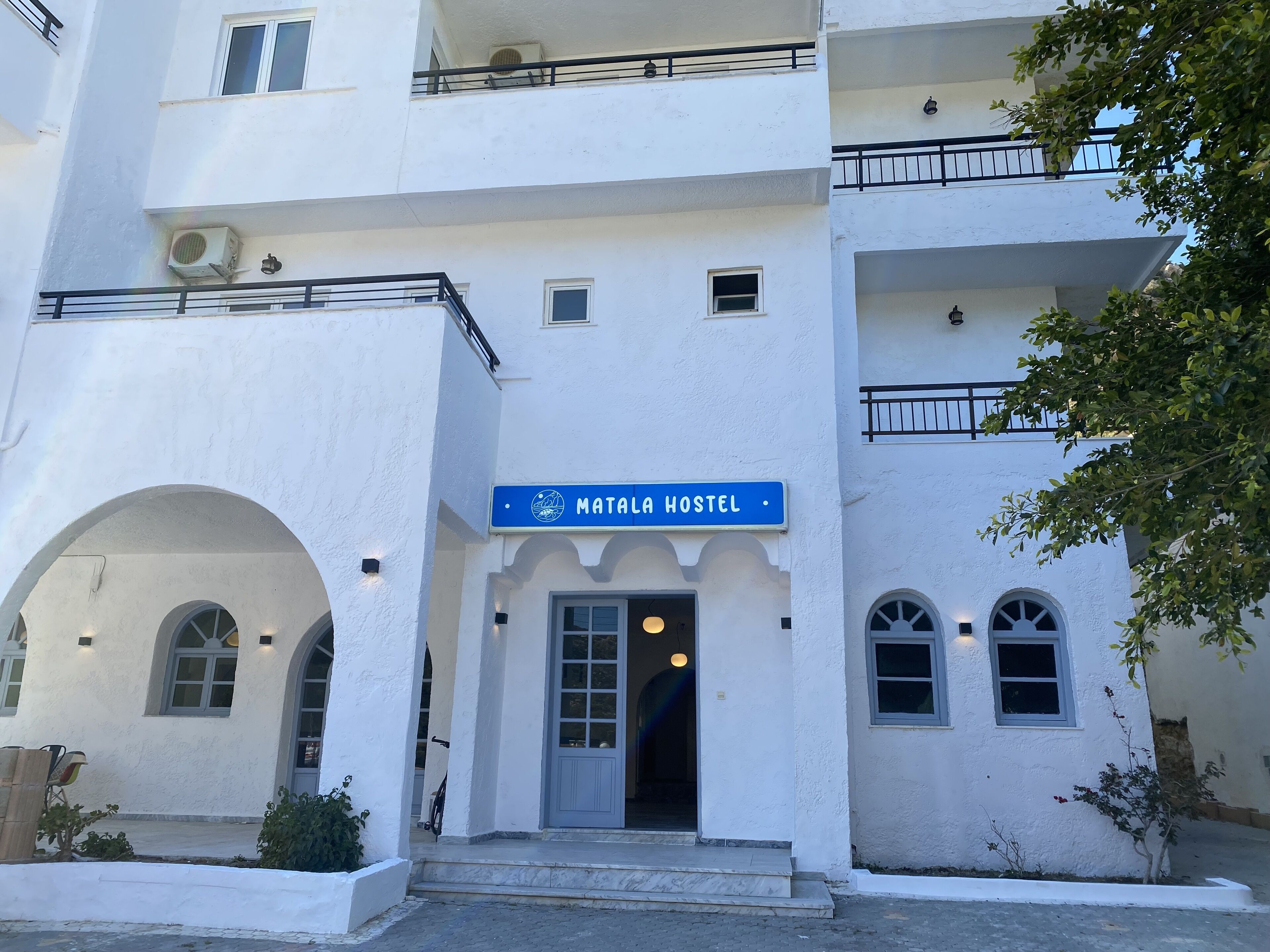 Un hostal llamado "Mata Hostel" con fachada blanca, múltiples ventanas y un cartel.