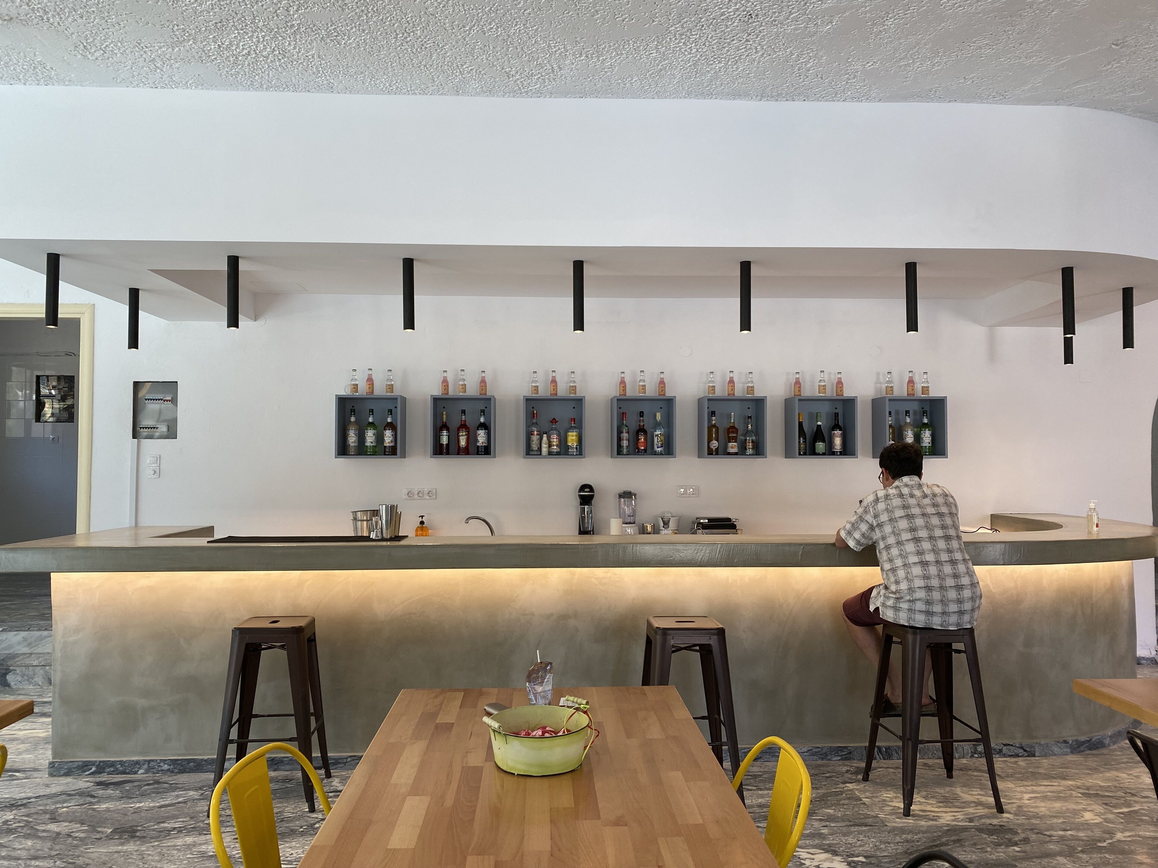 A modern bar area with a wooden counter, multiple shelves of bottles, and stools.