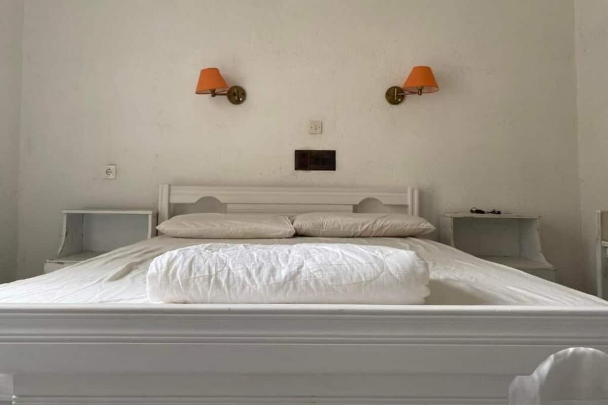 A bed with white bedding, two wall-mounted lamps, a small bedside table, and a nightstand.