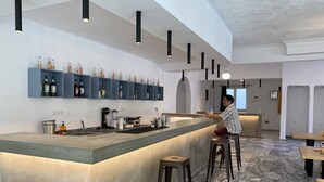A modern bar area with a long counter, stools, and shelves stocked with bottles.
