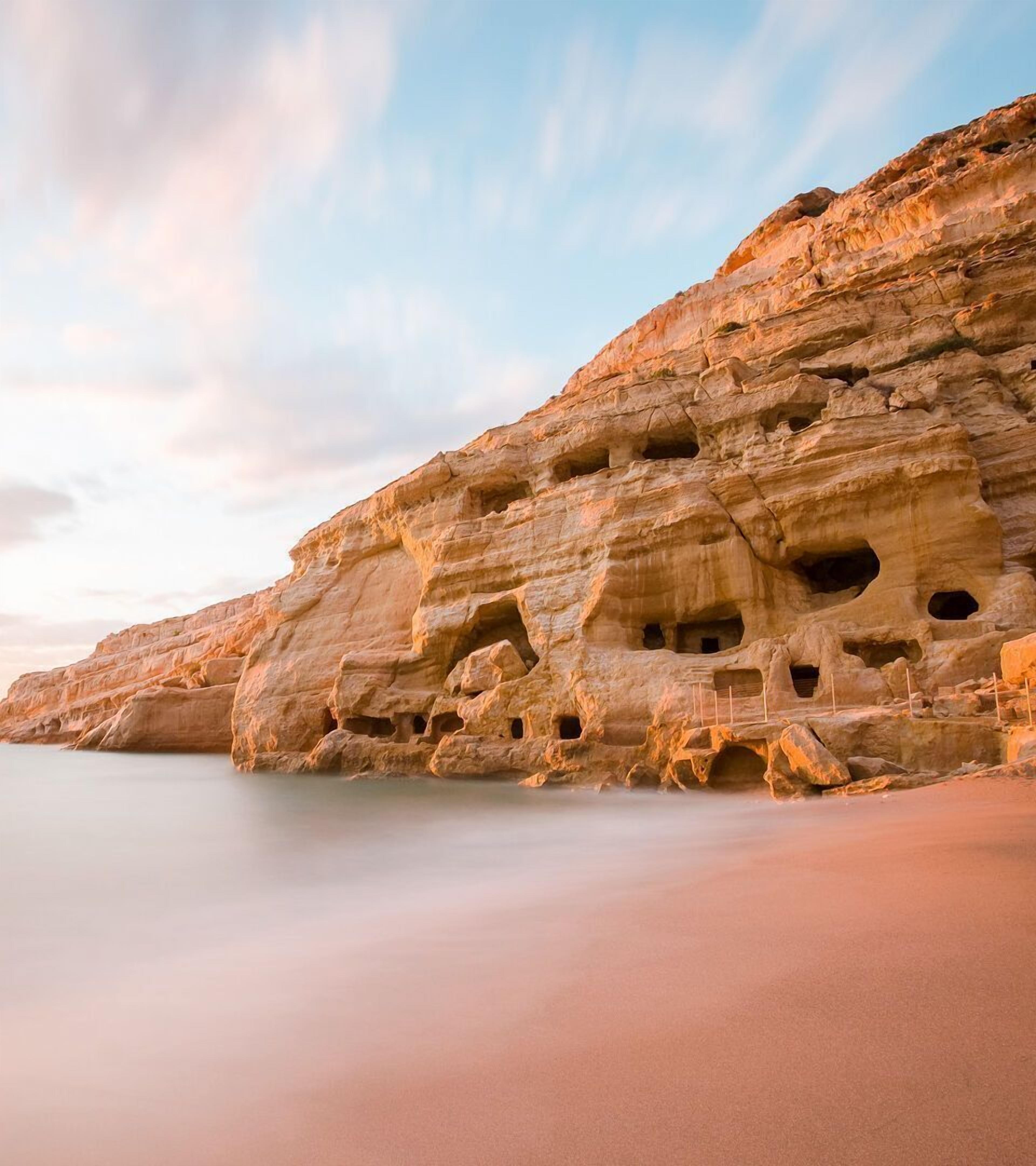 Un acantilado costero con múltiples cuevas y una playa arenosa.