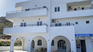 A modern hostel with a white facade, multiple balconies, and a sign reading "Matala Hostel".