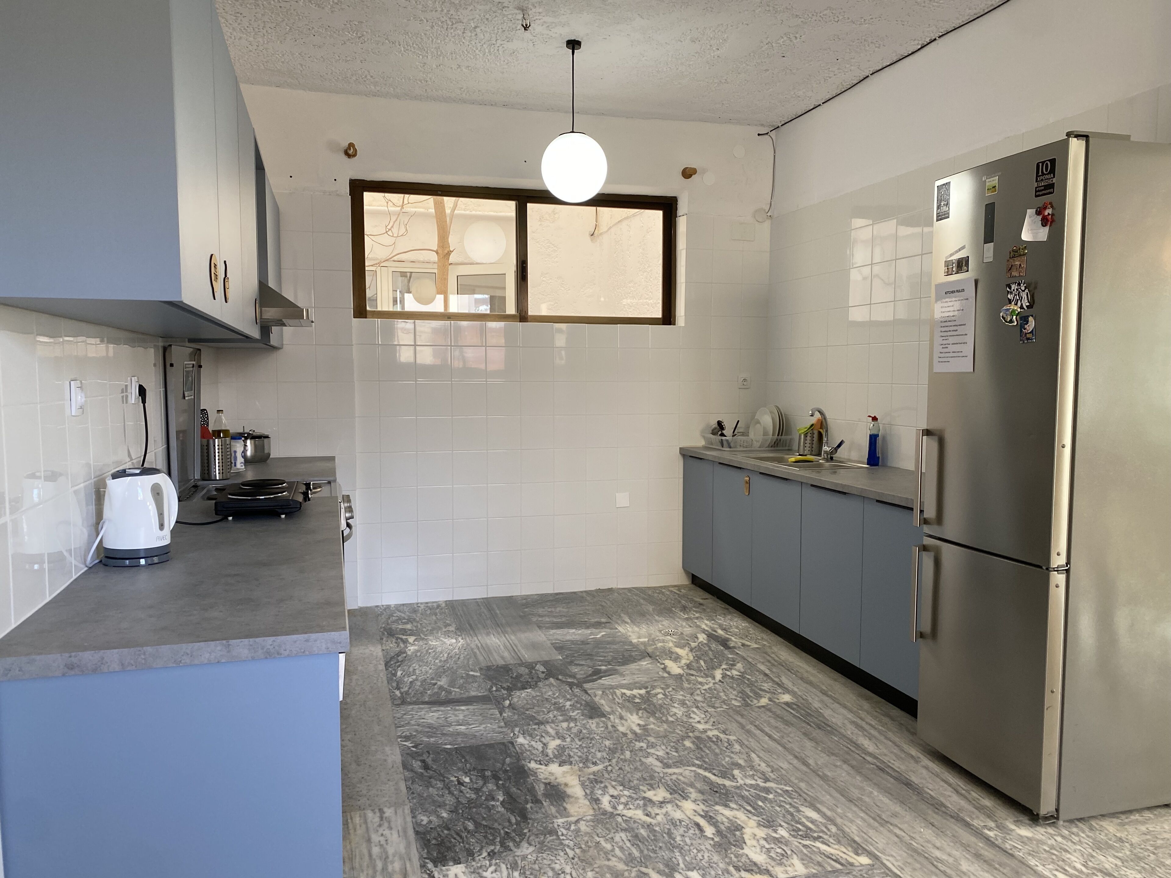 A modern kitchen with grey cabinets, a stainless steel refrigerator, and a marble-patterned floor.