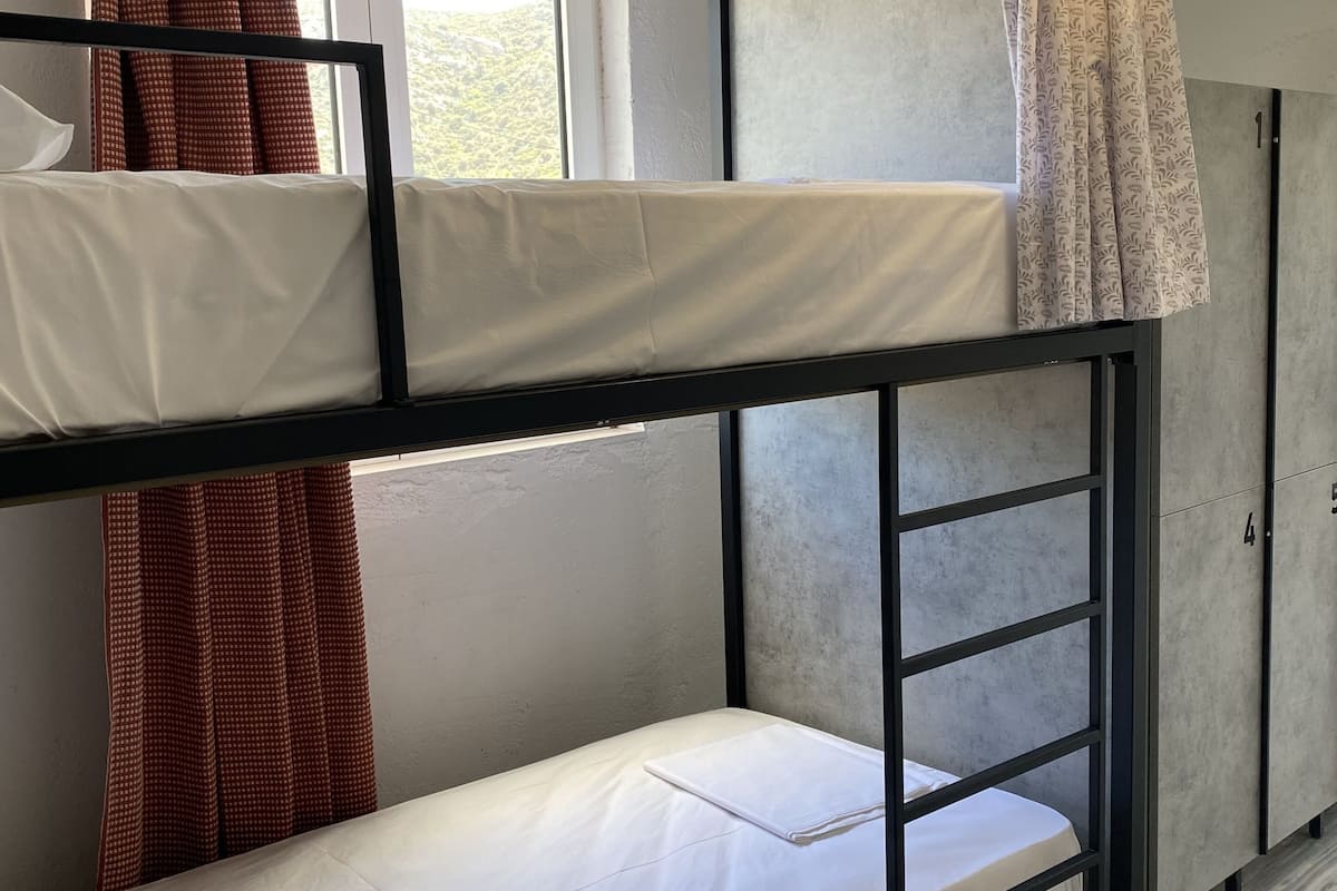 A bunk bed room with a window, curtains, and a hanging light fixture.
