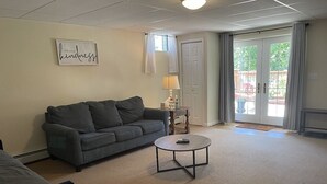 A living room with a grey sofa, a round coffee table, a lamp, and a door leading to an outdoor area. - Warwick Life - Leaf Peeping, Apple Picking, Skiing, Wineries, Breweries,Legoland (Warwick)