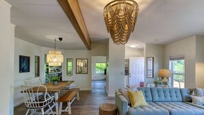 Un vaste espace de vie avec un canapé bleu, une table à manger en bois et des chaises blanches. Un grand luminaire tressé est suspendu au plafond, et des tableaux encadrés ornent les murs.