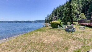 Une propriété située au bord du lac, dotée d’une pelouse, d’une petite terrasse avec des chaises et offrant une vue sur le lac et la forêt.