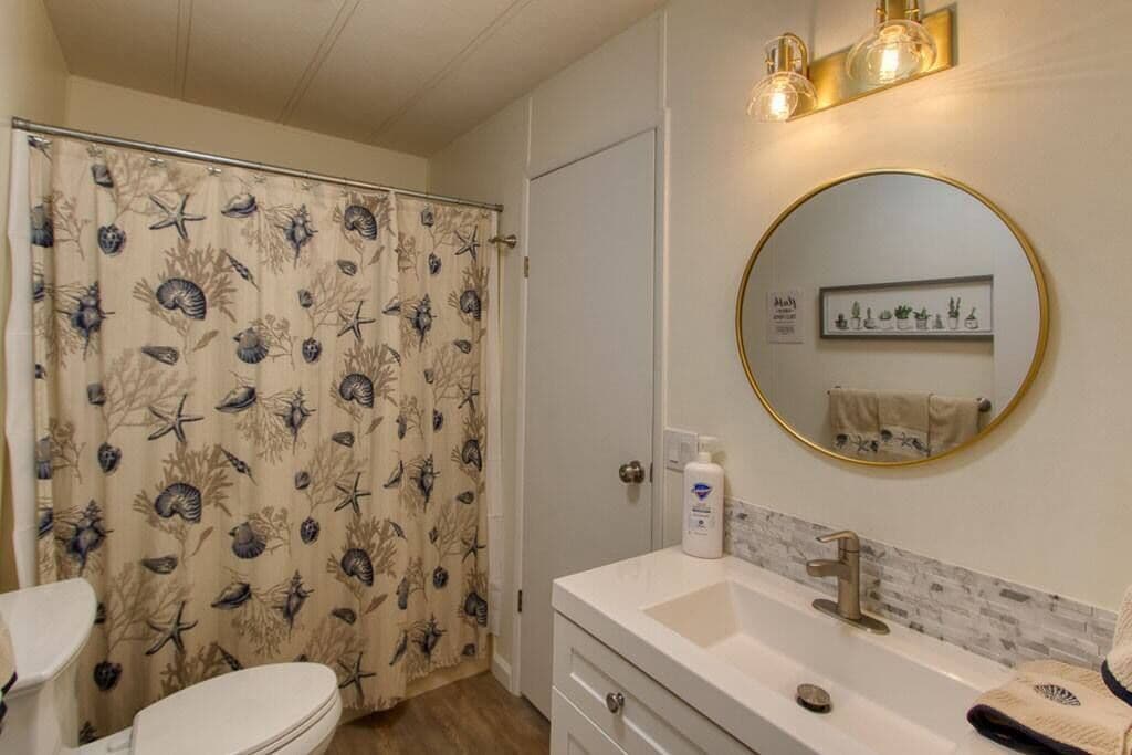Een badkamer met een douchegordijn met een zeedierenprint, een toilet, een wastafel met spiegel en een handdoekhouder.