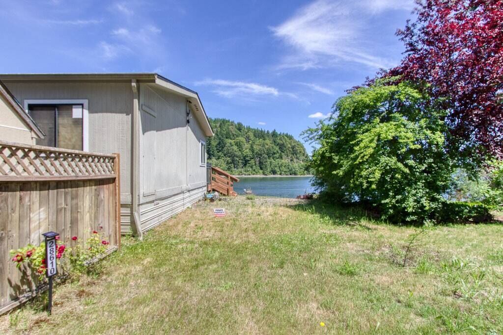 A single-story house with a fenced backyard, a small deck, and a view of a lake and forest.