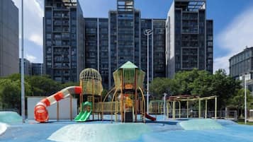 A playground with slides and climbing structures, surrounded by tall buildings.