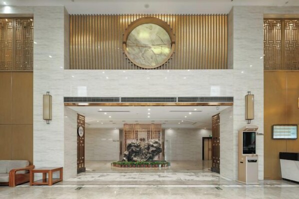 A hotel lobby with a reception desk, a large circular mirror, and a decorative fountain.