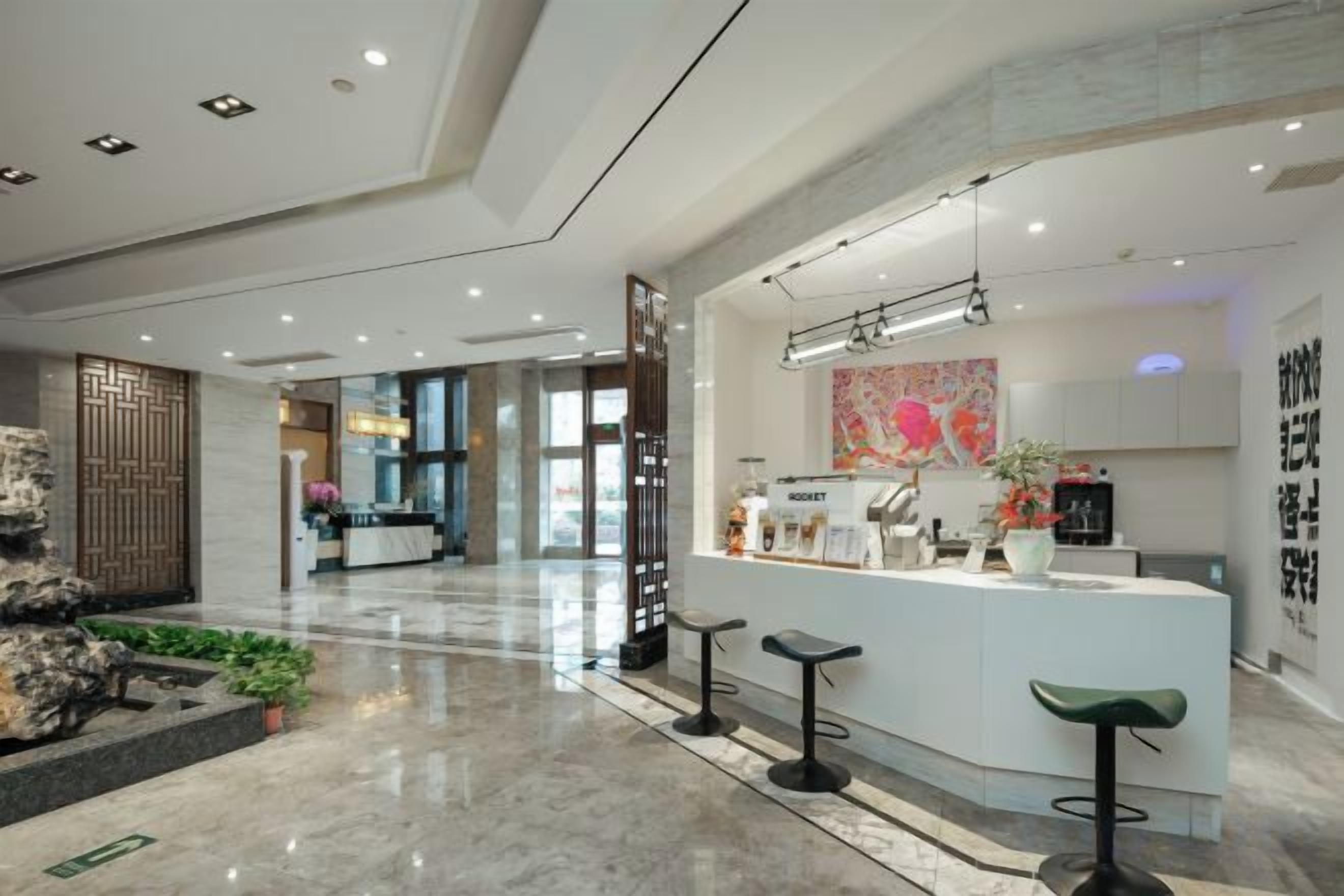 A modern hotel lobby with a reception desk, bar stools, and a decorative wall.