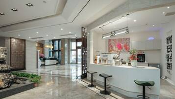 A modern hotel lobby with a reception desk, bar stools, and a decorative wall.