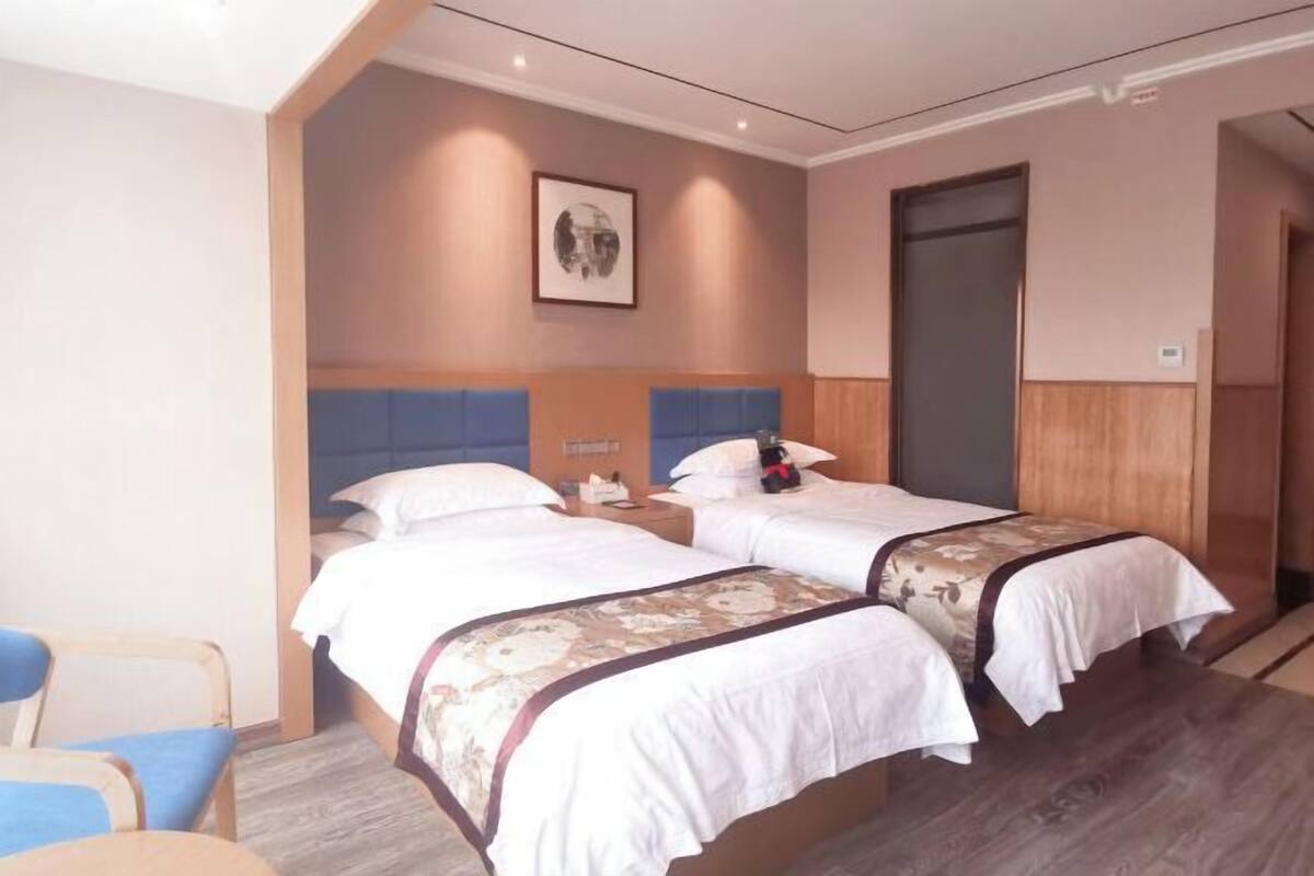 Habitació d'hotel amb dos llits, una cadira, una taula de nit i un quadre al mur.