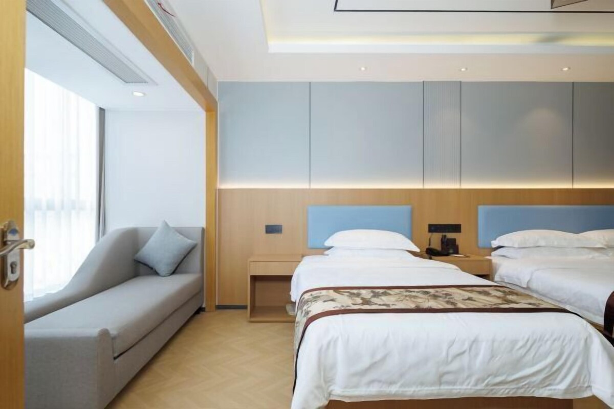 A hotel room with two beds, a sofa, a nightstand, and a large window.