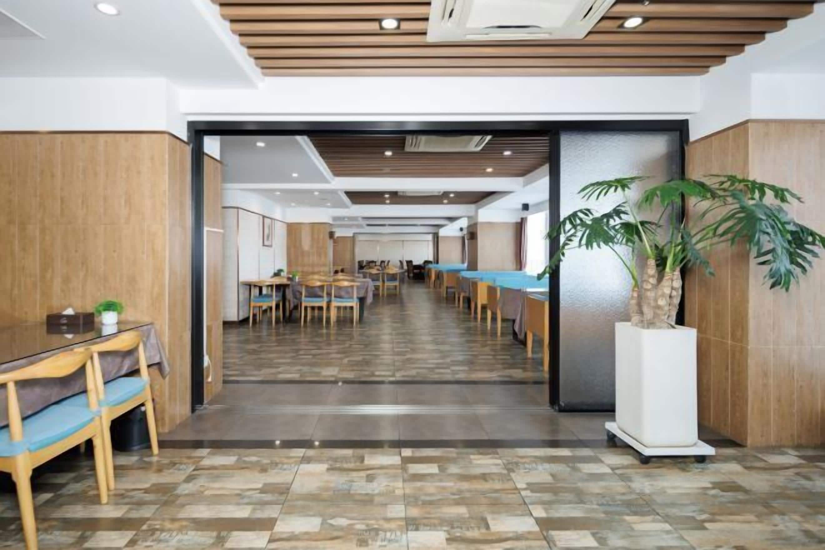 A hotel lobby with a long reception desk, multiple seating areas, and a large potted plant.