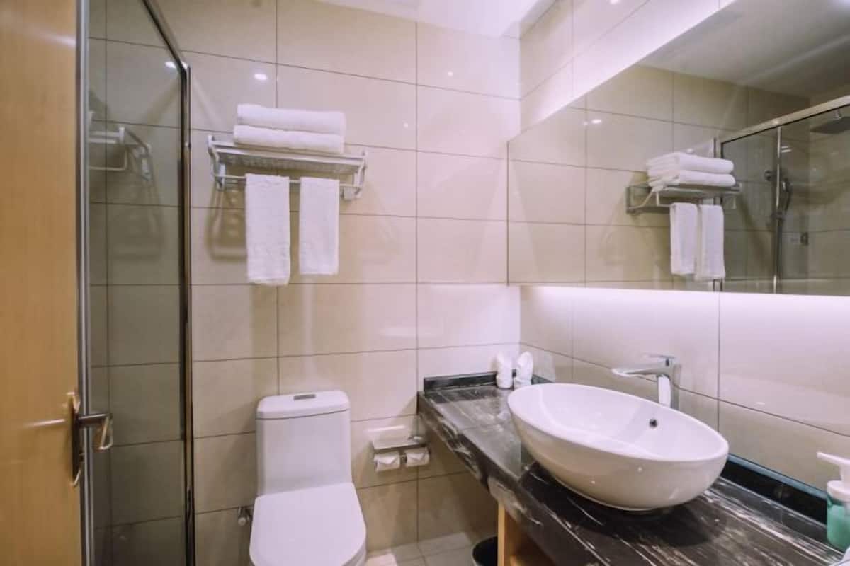 Un baño moderno con cabina de ducha de vidrio, inodoro blanco, encimera de mármol y un espejo grande.