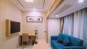 A compact hotel room with a desk, a blue sofa, a television mounted on the wall, and a framed picture above the desk. - Jia Yue Hotel (Tongxiang)
