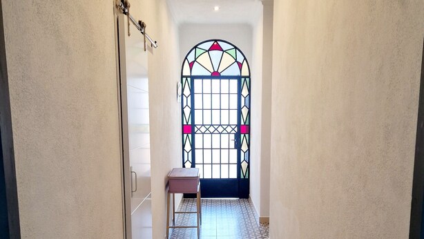 A hallway with patterned flooring, a bench, and a door leading to a room with a stained glass window. - Vrbo Property (Encinasola)