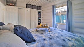 Een slaapkamer met een bed, een kledingkast, een dienblad met ontbijtartikelen en een raam met gordijnen.