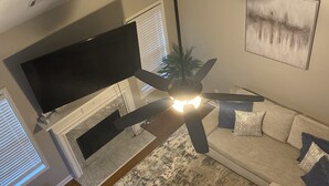Una sala de estar moderna con un sofá seccional, un televisor de pantalla plana y un ventilador de techo.