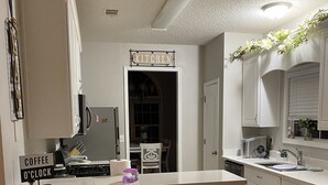 Una cocina con barra, armarios blancos, un letrero de café y un reloj.