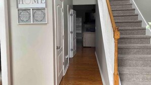 Un pasillo con una escalera que conduce a un segundo piso, una puerta con la leyenda "HOME" y un cartel enmarcado con texto.