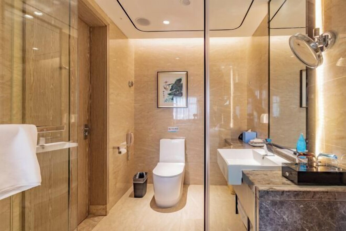 A modern bathroom with a glass shower enclosure, a toilet, a sink with a mirror, and a framed artwork on the wall.