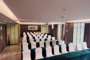 Un salón de conferencias con filas de mesas y sillas, un proyector y un amplio ventanal.
