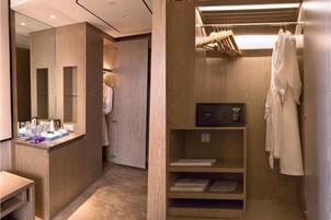 A modern bathroom with a wooden vanity, a mirror, a robe hanging, and a shelf with toiletries.