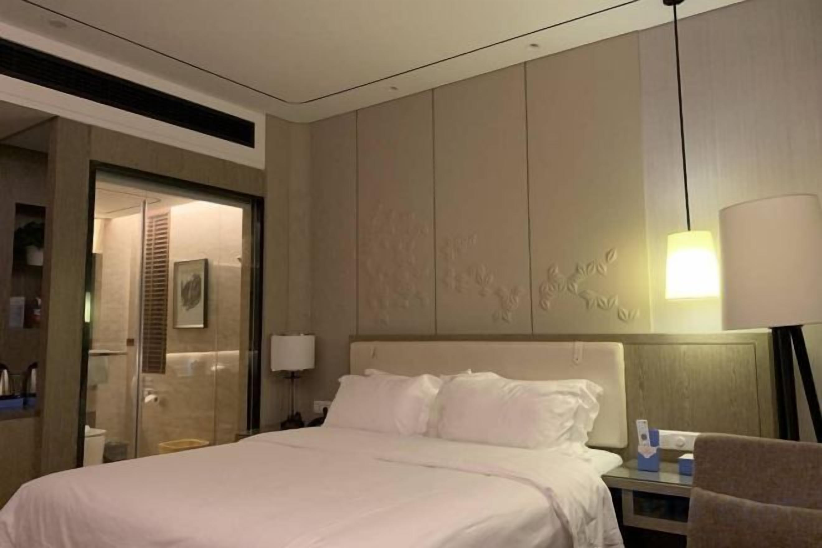 Habitación de hotel con una cama grande, una mesita de noche, una lámpara y un aplique de pared.