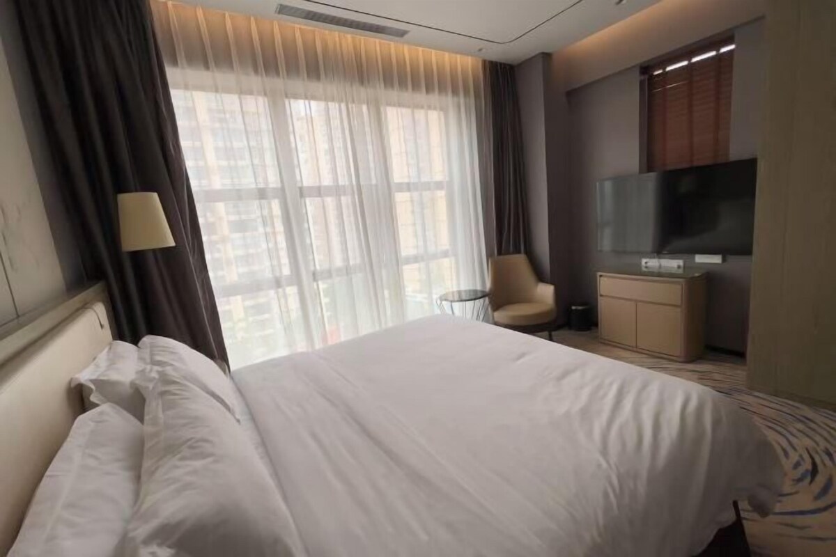 A hotel room with a large bed, a TV, a chair, and a desk.