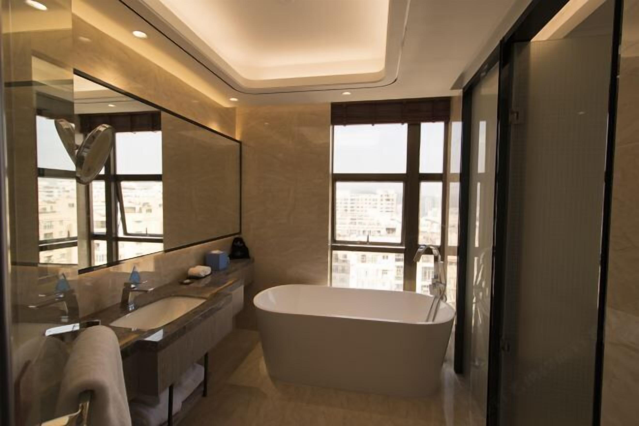 A modern bathroom with a large bathtub, a vanity with a mirror, and a view of the city through large windows.